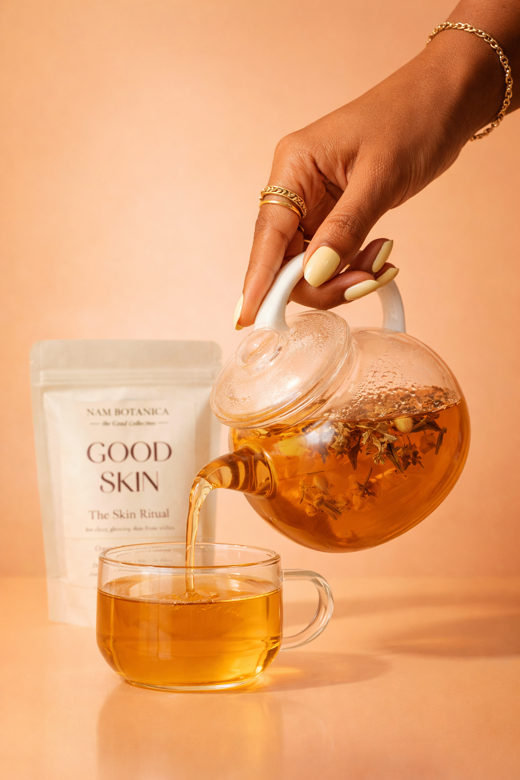 Woman pouring Nam Botanica Good Skin Tea from a glass teapot into a clear cup, with product pouch in background